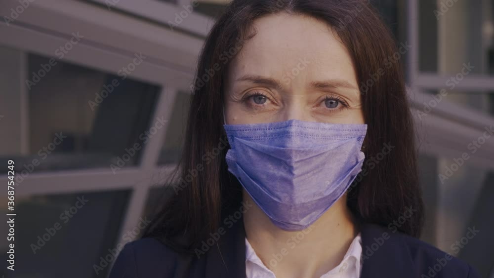 A young woman doing business wears a medical face mask to avoid the spread of coronavirus in the street. A close-up steadycam shoot of a lady with a surgical mask on the face against COVID-19. A young woman doing business wears a medical face mask to avoid the spread of coronavirus in the street. A close-up steadycam shoot of a lady with a surgical mask on the face against COVID-19.
