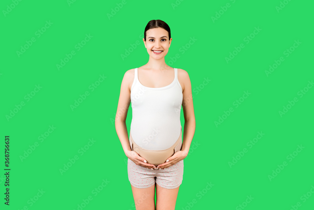 Portrait of pregnant woman using pregnancy belt at green background with copy space. Orthopedic abdominal support belt concept Portrait of pregnant woman using pregnancy belt at green background with copy space. Orthopedic abdominal support belt concept