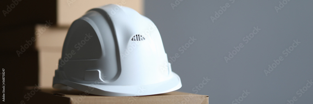 Fototapeta premium Cardboard box lies white protective helmet builder. Providing workers with personal protective equipment. White helmet for head or public inspector. Compliance by employees with safety regulations