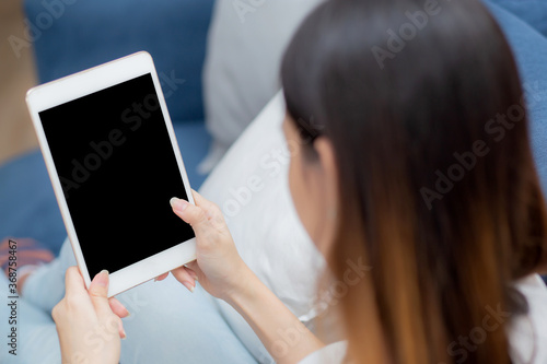 Closeup young asian woman sitting and using mockup of tablet computer with display blank screen on sofa at home, girl holding digital tablet watch entertainment at living room, communication concept.