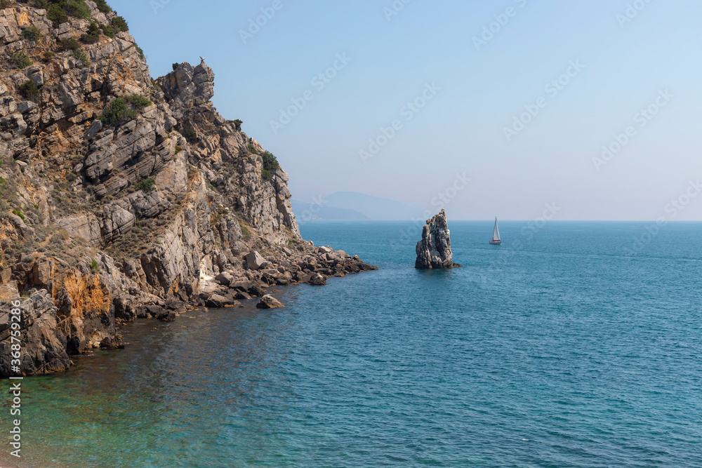 Rock Sail, Yalta, southern coast of Crimea. A sailing yacht sails next to a rocky shore on a sunny summer day. Travel adventure, yachting