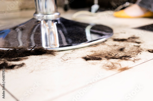 Cut brown hair lying on floor near metal barber chair. Saloon need cleaning service