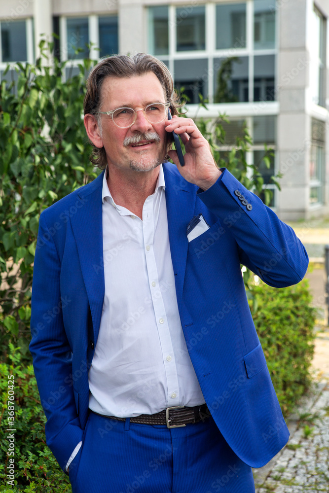 businessman in his 50s standing outside and talking on the phone businessman in his 50s standing outside and talking on the phone