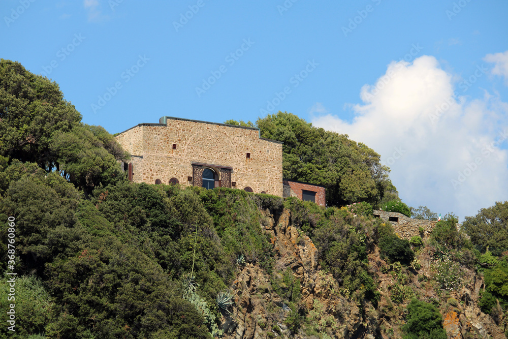 Casa in pietra su rilievo roccioso fra pini e agave
