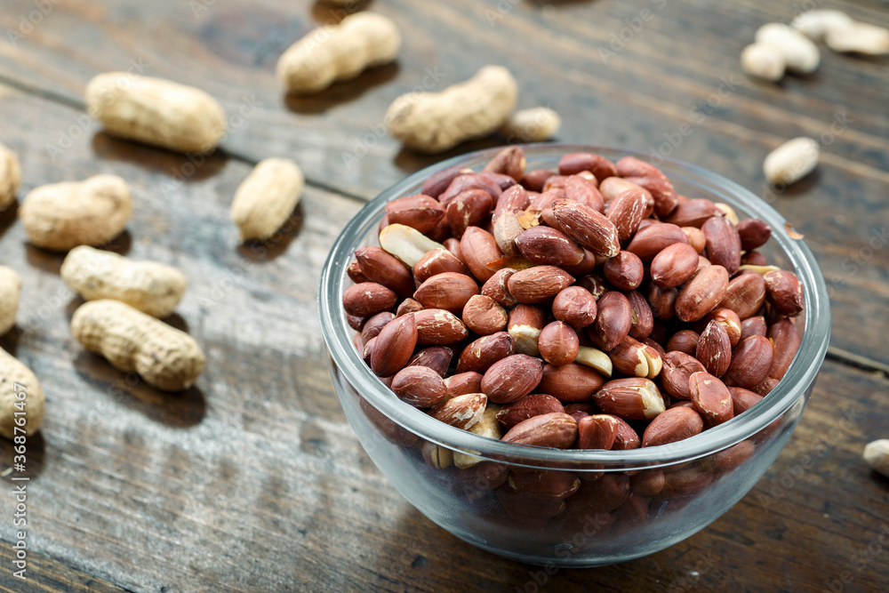 unshelled peanuts in a glass plate on a wooden background. peeled peanuts are scattered nearby. traditional beer snack. place for text. unshelled peanuts in a glass plate on a wooden background. peeled peanuts are scattered nearby. traditional beer snack. place for text.