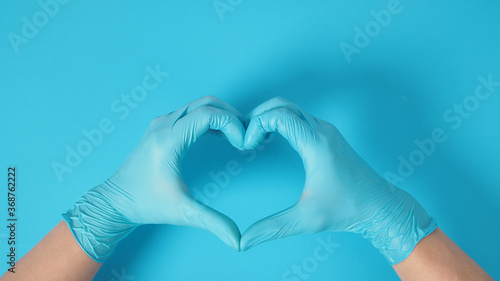 A Hand is doing love hand sign and wear surgical gloves or latex gloves on blue background.