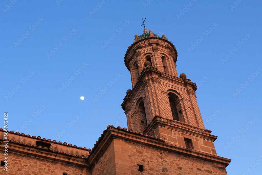 The moon appears over the bell tower