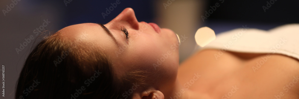 Fototapeta premium Close-up of relaxed young woman laying on table in spa center. Relaxing massage and body care procedure. Soft lights and comfort for client. Wellness health and beauty concept