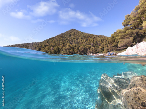 Underwater and sea level photo of amazing tropical rocky turquoise clear seascape with caves and natural pine trees