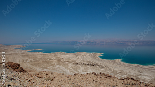 Dead sea landscape wide angle shot. Dessert terrain with sinkholes in the foreground and mountains of Jordan in far background.