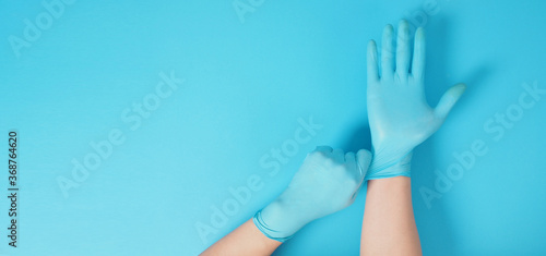 The hand is pulling doctor gloves or blue latex gloves of right hand on a blue background.