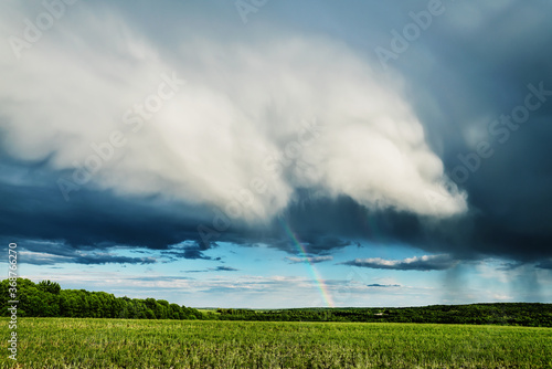 Rainclouds and rain over a field with rainbow