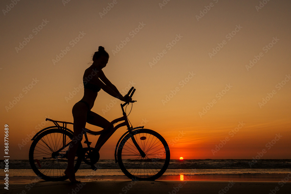 Fototapeta premium healthy alone woman ride on bicycle on empty sunset Goa India beach