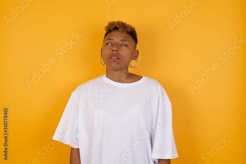 Tableau sur toile YYoung African American girl with afro short hair wearing white tshirt standing over isolated yellow wall looking sleepy and tired, exhausted for fatigue and hangover, lazy eyes in the morning