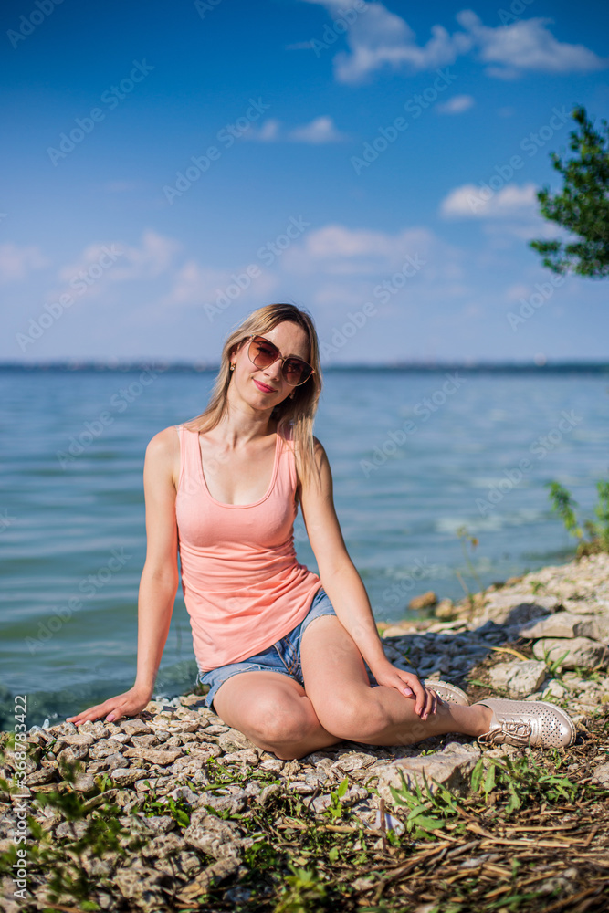 A girl sits on a rocky lake shore on a sunny day