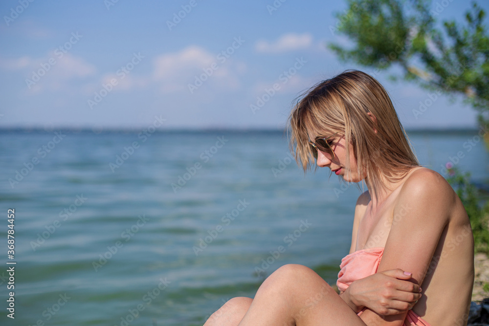 A girl sits on a rocky lake shore on a sunny day