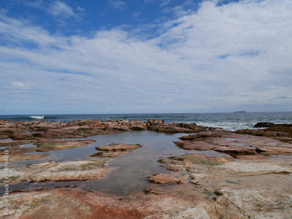 rock formations on the seashore with water, white clouds and blue sky