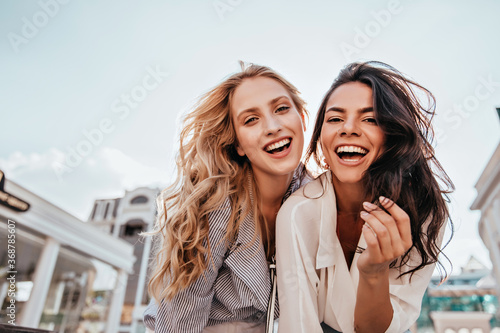 Appealing long-haired girls posing on sky background. Laughing ladies enjoying weekend together. photo