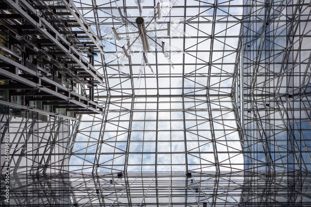 View from below on glass roof in building. Abstract background. Clouds on the sky are visible through glass.