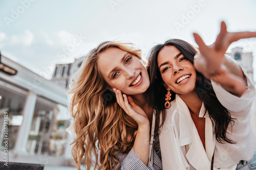 Good-humoured caucasian ladies posing with smile on sky background. Outdoor shot of dreamy female models spending weekend together.