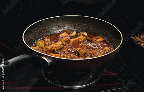 chicken curry is prepared in a pan on a stove.