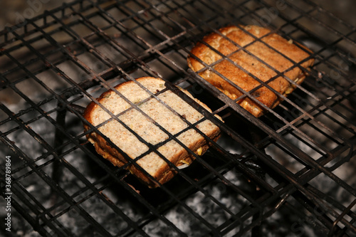 Sandwiches being cooked using a braai grid and hot coals. This photo has selective focus. 