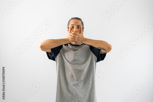 Hombre con pelo recogido y camiseta gris de mangas azules se tapa la boca con las dos manos