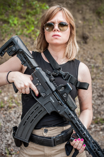 Attractive female army soldier hold rifle machine gun. Woman with weapon. Firearm outdoor shooting range