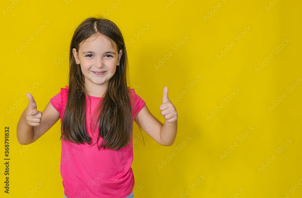 A little cute happy girl, looking at the camera and showing a sign of approval, class, on a yellow background. A little cute happy girl, looking at the camera and showing a sign of approval, class, on a yellow background.