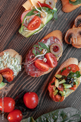 various beautiful bruschettas with vegetables, avocado, salami, cheese, tomatoes, guacamole, olives and radishes on the 