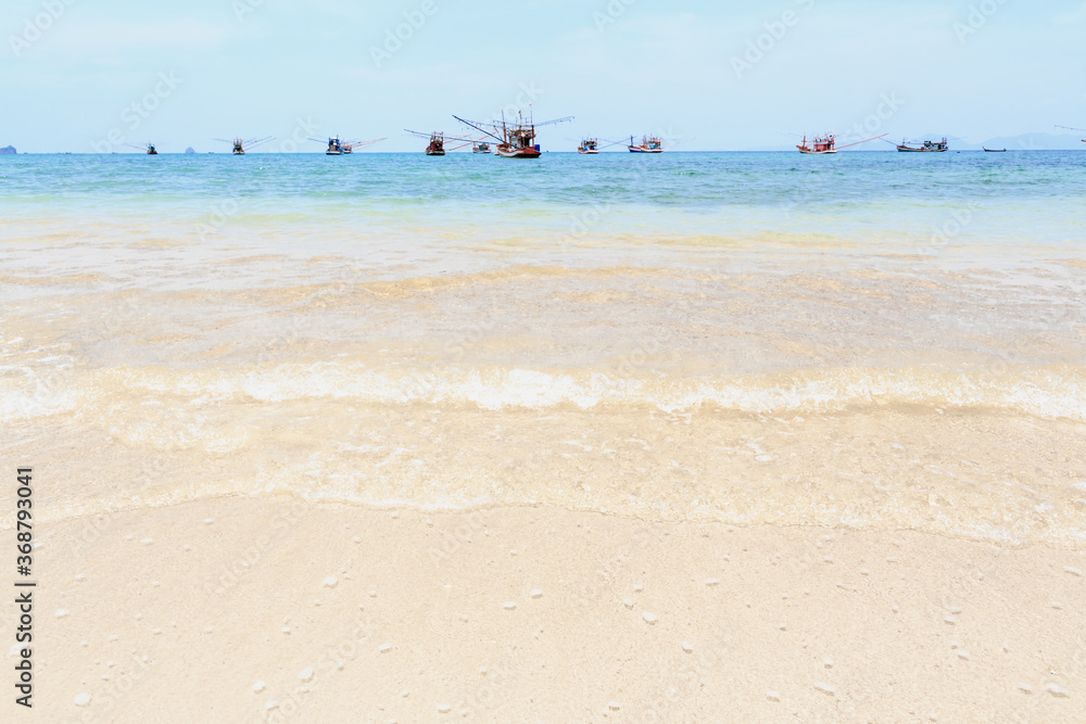 The waves had a clean white bubble lapping the sandy beach, With the backdrop of a group of fishing boats.There is an island behind. The clear blue sky in the summer is perfect to travel.