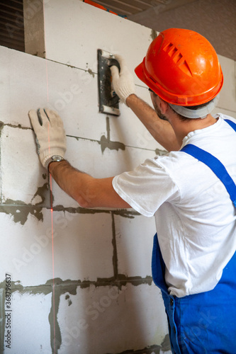 Mason aligning aerated autoclaved concrete block of constructed house wall