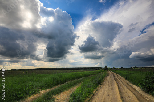 Country road in the field with a cloudly sky