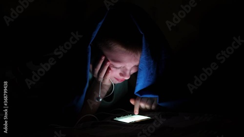 young children using cell phone hidden under bed covers. The child listens to music and looks at the photos