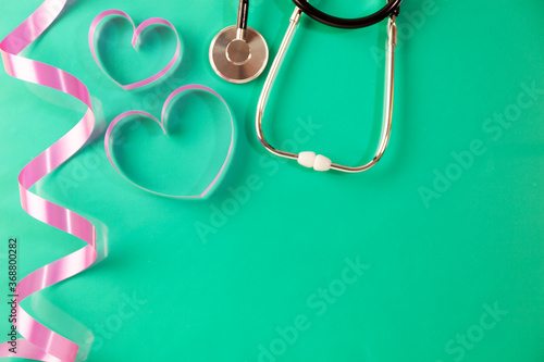 Stethoscope with heart ribbon on green paper background copy space for your text.
