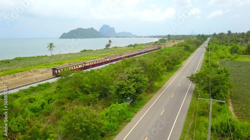 aerial view, Train run on rialroad track parallel roads surrounded with plants near the sea. photo