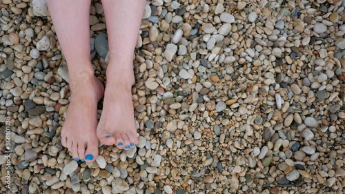 Female feet on the shallow beach. View from above. The girl lies on the beach. Copy space. Sea stones. Pebbles. Seaside.