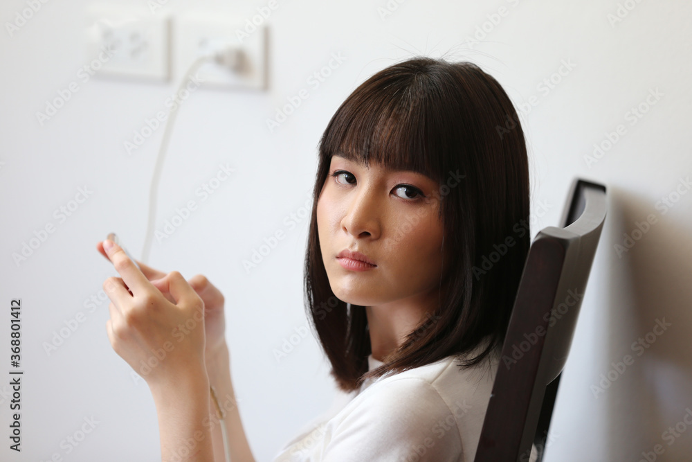 young woman texting on mobile phone while charging power on wall. young woman texting on mobile phone while charging power on wall.
