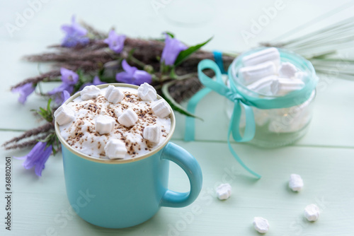 Hot chocolate with whipped milk froth and marshmallows in a blue Cup. On a turquoise background.