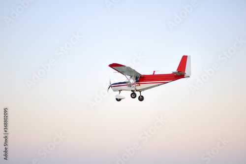 Small ultralight airplane with overhead wing and single propeller flying in sky. Such aircraft are used for recreational, sport and flight training.