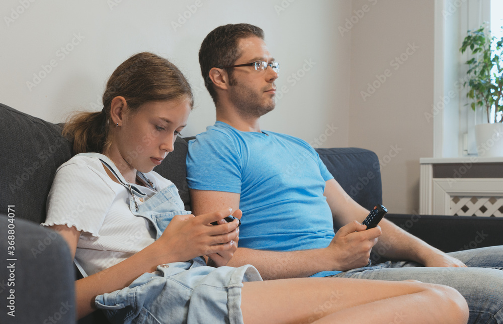 An ordinary modern family. Dad watches TV, daughter plays on the smartphone. An ordinary modern family. Dad watches TV, daughter plays on the smartphone.