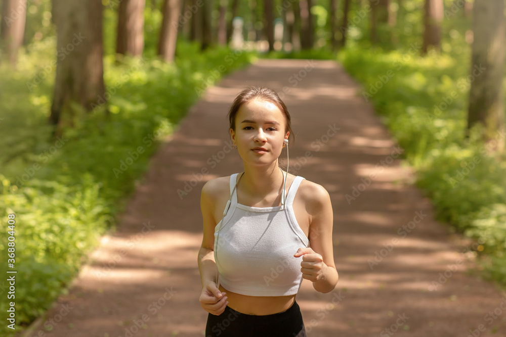 Exercise in the fresh air. Girl runs in headphones in the park among the trees Exercise in the fresh air. Girl runs in headphones in the park among the trees