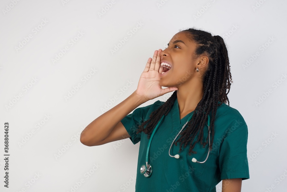 young doctor woman, standing against yellow background profile view, looking happy and excited, shouting and calling to copy space. young doctor woman, standing against yellow background profile view, looking happy and excited, shouting and calling to copy space.