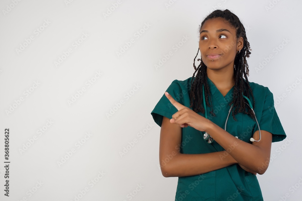 Obraz premium Pretty doctor woman posing on camera with tricky look and gesturing to side. Female designer presenting lovely product with index finger. Gesture concept.