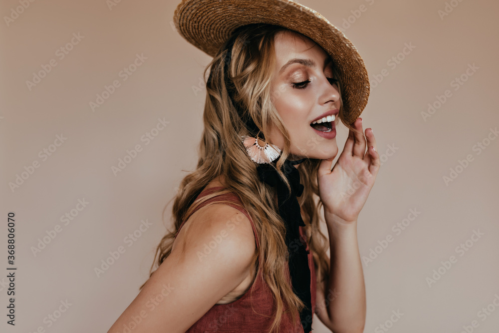Long-haired blissful lady in canotier posing on brown background. Studio shot of dreamy curly girl wears boater hat. Long-haired blissful lady in canotier posing on brown background. Studio shot of dreamy curly girl wears boater hat.