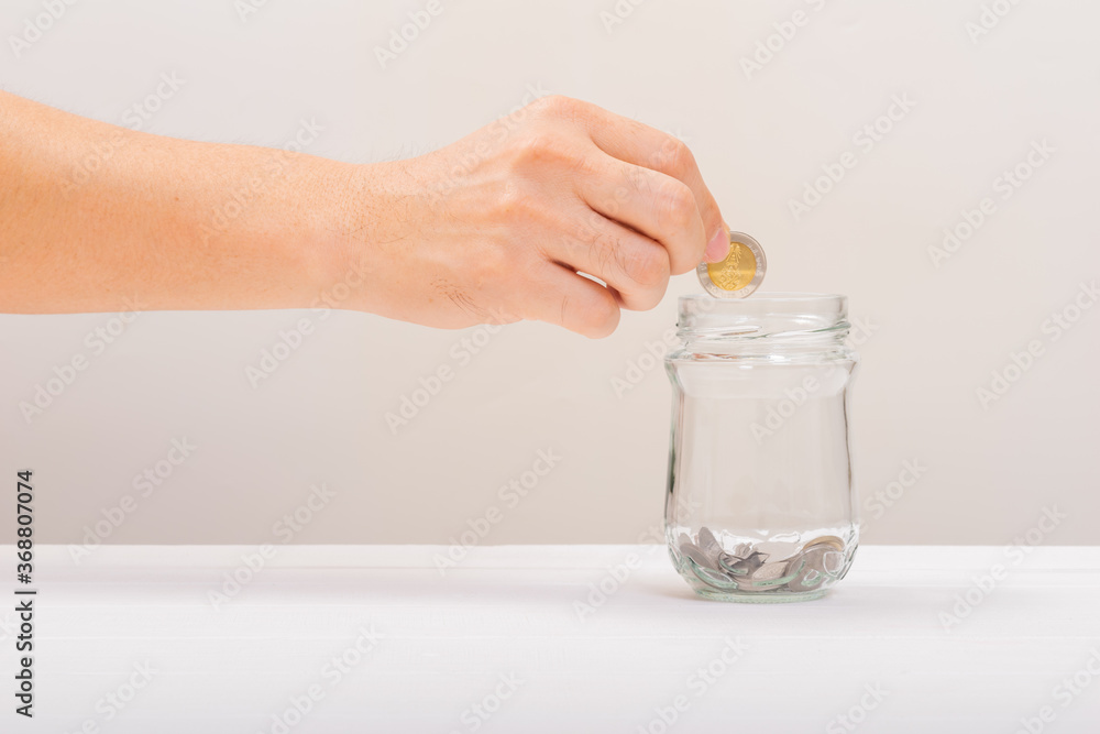 White hand man holding coin to putting in Jar or glass bottle for saving with soft white background. Saving money, Saving concept White hand man holding coin to putting in Jar or glass bottle for saving with soft white background. Saving money, Saving concept