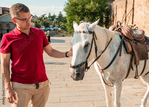 Close up male with a horse in the background of city streets. Happy man in red shirt with an animal horse. Friendship, animal and people