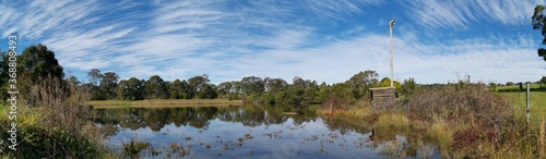 Beautiful afternoon panoramic view of a peaceful pond in a park with reflections of deep blue sky, light clouds and trees on water, Fagan park, Galston, Sydney, New South Wales, Australia