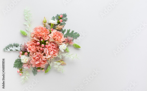 Flowers composition made of coral carnation and silver-green leaves of Senecio cineraria on pastel grey background. Nature concept, copy space, flat lay.