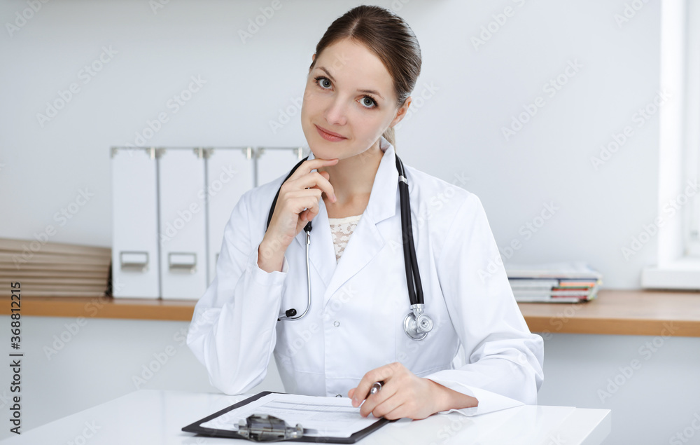 Woman-doctor sitting and working at clinic office. Portrait of female physician. Medicine concept Woman-doctor sitting and working at clinic office. Portrait of female physician. Medicine concept